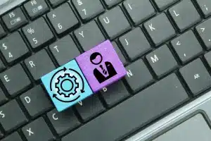 Dos cubos de colores con iconos de engranaje y persona sobre un teclado de ordenador.